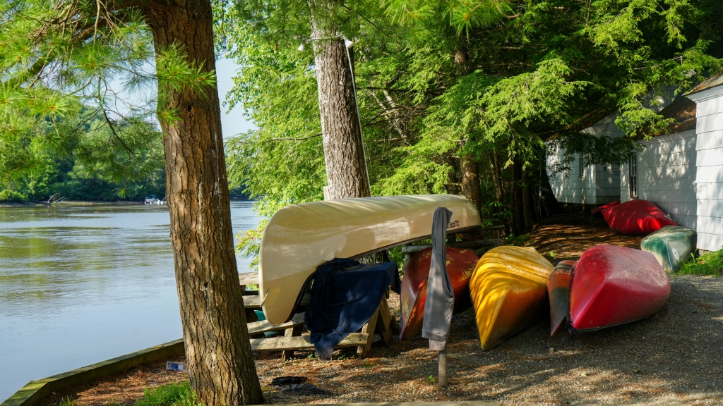 Canoes are stacked on the bank of a river.