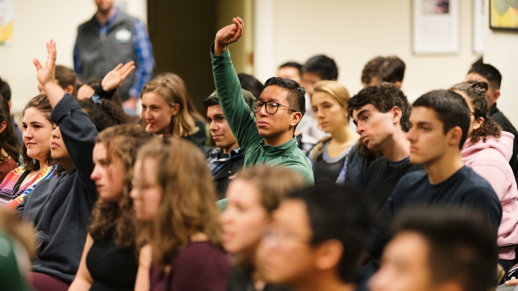 Three rows of students attend a presentation at the Center for Professional Development (CPD), with two students seated towards the middle raising their hands. A CPD employee stands behind the students, observing.